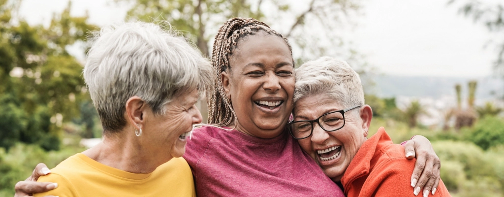 Three older women hug while laughing